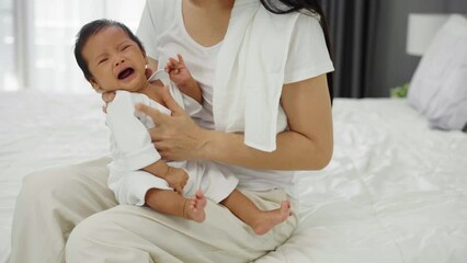 mother holding burping and crying baby in a bedroom after feeding milk