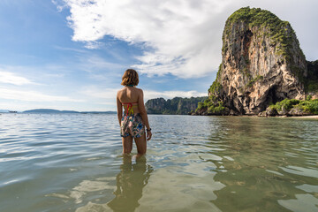 Traveler woman in turquoise water looking towards the Phra nang Cave on a summer day. Thailand