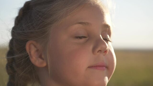 Child's face close-up in fresh air in the park. girl stands with closed eyes dreaming upward. Happy emotions of child. girl enjoys happiness with her eyes closed. Dream concept in park
