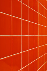 The wall is clad in modern orange glossy ceramic tiles with white grout. Angle view. Selective focus.