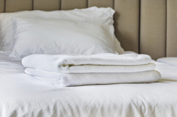 Fototapeta na wymiar White towels on bed in guest room for hotel customer. folded terry towels lies on clean white bed.