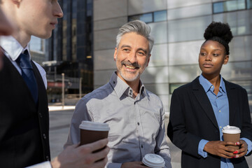 diverse coworkers drinking coffee in buildings, focus on mature gray haired man.
