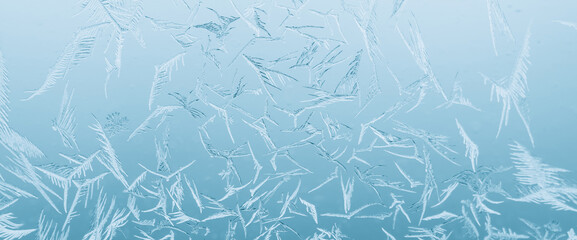 Minimal light backdrop with icy crystals on window in day light. Frosty texture on glass closeup in blue light. Blurry minimalist monochrome background of icy pattern on frozen window glass close up.