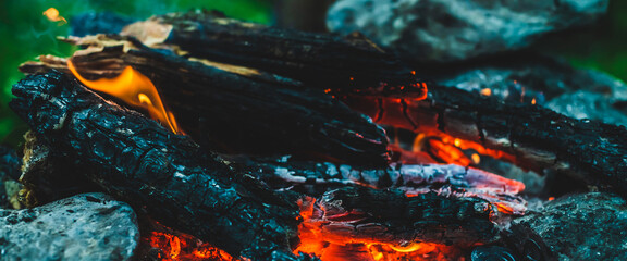 Vivid smoldered firewoods burned in fire close-up. Atmospheric warm background with orange flame of...