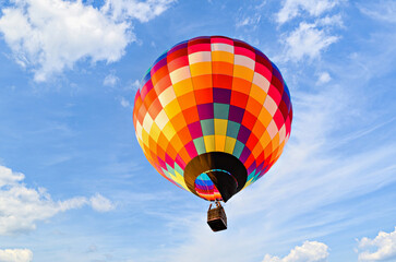 Colorful hot air balloon flying over blue sky with white clouds	