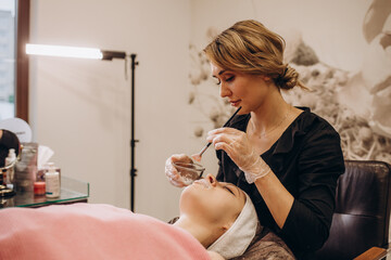 Cosmetologist wearing a mask and gloves applies permanent makeup to the lips of a young girl