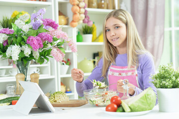 Obraz na płótnie Canvas girl preparing fresh salad on kitchen table with tablet at home