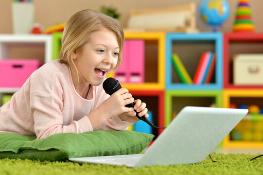 Adorable little girl singing karaoke with laptop