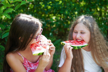   Close up portrait of two young girls laughing, eating  and enjoying a watermelon.