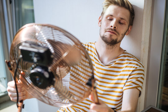 Heat wave during a summer, a man finds respite at his home balcony with the help of an electric fan. A man beats the summer heat wave by finding relief with an fan. The effect of global warming
