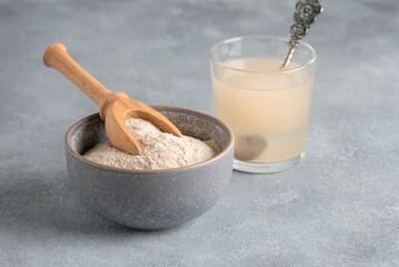 Psyllium husk powder in bowl closeup and glass with of water soluble fiber for intestinal, gray...