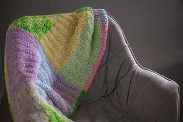 Knitted multi-colored plaid. A knitted blanket on the chair. Home interior. Cozy home comfort....