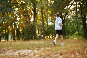 a caucasian girl in a blue sweatshirt puts on headphones in the park and prepares to run. pretty young woman puts on headphones. Pretty smiling woman puts on headphones in the park before jogging.