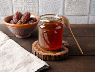 Natural organic healthy date syrup in a glass jar with whole dates and wood spoon on the background