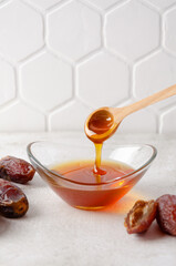 Natural organic healthy date syrup flows from wood spoon into a glass bowl with whole dates on the...