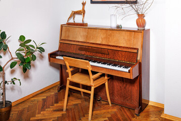 An old piano in the corner of the room against a white wall.