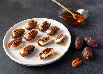 Snack set (starters, appetizers) with dates, brie or camambert cheese, pecan nuts and natural organic homemade date syrup for healthy bite through on the background. Selective focus