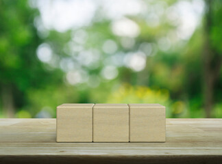 Three wood block cubes on wooden table over blur green tree in park
