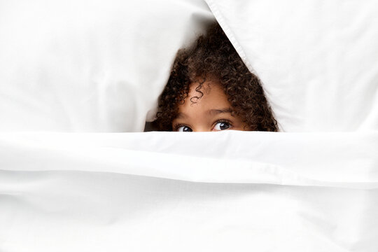 Little girl's eyes peeking from white sheet