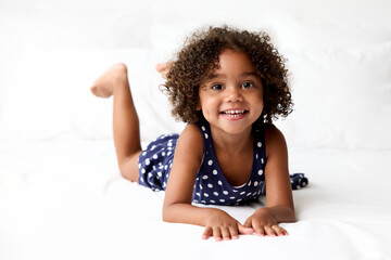 Happy young girl with afro hair lying on stomach on white bed
