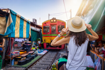 Naklejka premium A tourist woman on sightseeing tour visits the famous train and railway market in Maeklong, Thailand, during early morning hours