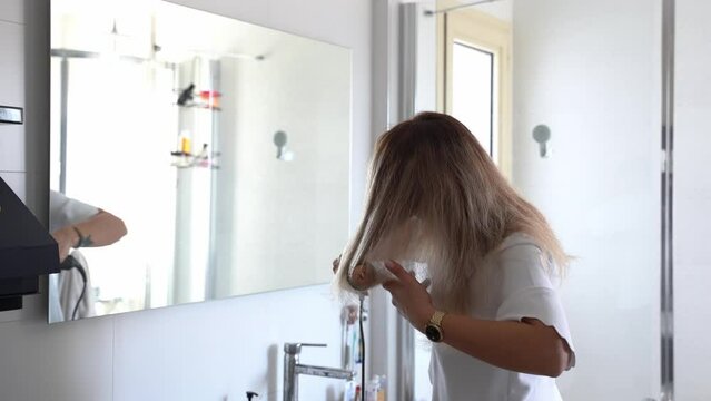 Woman styling hair with dryer styler care machine in bathroom. Young female using a modern rotative hair brush to style her hair. Thermal and ceramic coating rotating brush with attachments