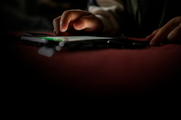 スマホ依存症、スマホ中毒の子供の手のイメージ。真っ暗な寝室でスマホやスマートウォッチを取る子供の手。