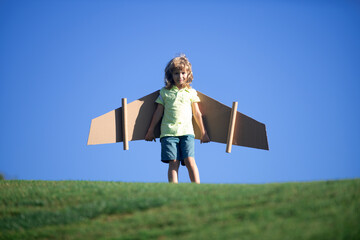 Portrait of cute blond child play pilot with handmade craft paper plane wings. Kids dreaming, success, creative and startup concept.