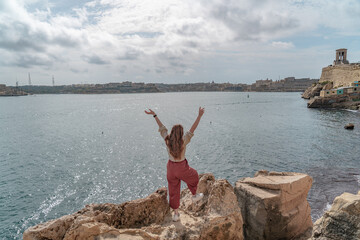 Woman standing on rocks at the harbor of Valletta