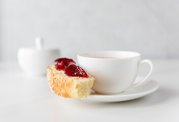 White cup of coffee with roll and jam