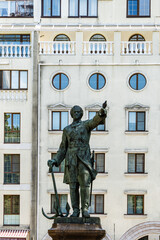 Obraz premium Bronze statue of king is mounted on pedestal made of pink Pavlovsk granite. Monument to Peter I in Petrvsky Square. Ship guns near monument. Fountain in background. Voronezh, Russia - July 30, 2022