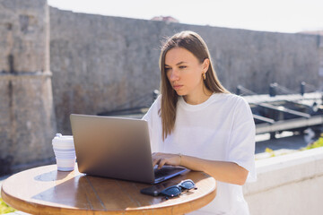 Portrait of a young woman who is concentrating on her laptop on a summer terrace. Managing your business remotely