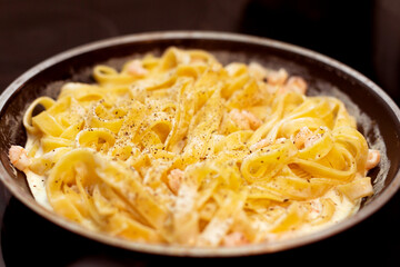 Tagliatelle pasta with shrimps with sauce in frying pan. Cooking Italian dish