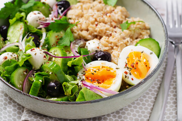Breakfast oatmeal porridge with boiled eggs, cucumber, mozzarella cheese and green herbs. Healthy balanced food.