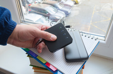 Person holds Portable 3g 4g mobile wireless internet router with power bank on window at home. To...