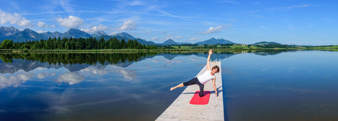 Junge Frau bei Pilates-Übungen in der Natur, Balance-Schulung und Muskelkräftigung auf einem Steg...