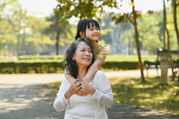 Naklejka premium Happy moments with grandmother and little granddaughter walking in the park surrounded by green trees at sunlight morning
