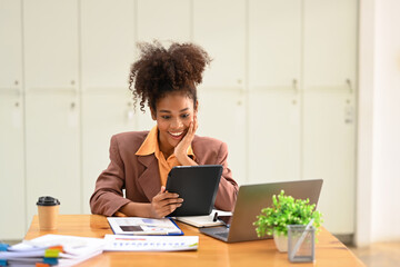 Smiling female financial advisor using tablet for checking information or chatting online with her client