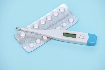 Electronic modern thermometer with pills in a blaster pack on a blue background