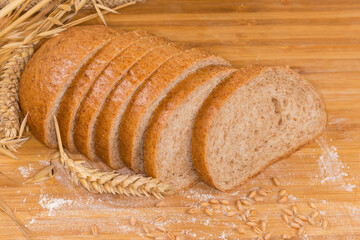 Sliced bread with bran among ears, wheat grain and flour