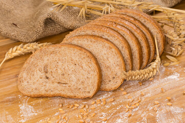 Sliced bread with bran among ears, wheat grain and flour