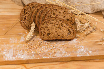 Sliced brown bread among different ears, wheat grain and flour