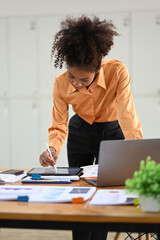 Concentrated African American accountant stating at her workplace and checking online information on digital tablet