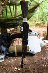 An automatic rifle near a tent in the forest, a military tent in the forest during the war in Ukraine.