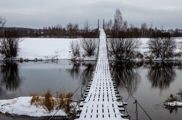 Suspension bridge in winter day. Bridge to the other side of the river for pedestrians.