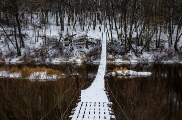 Wooden bridge across the river in the countryside. Suspension wooden bridge in winter.