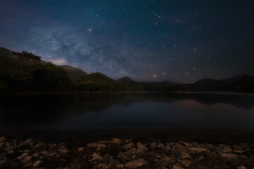 Milky way over Mae Pha Haen Reservoir with mountain view at night. On Tai, San Kamphaeng District, Chiang Mai. Thailand.