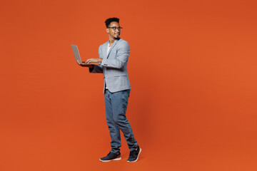 Full body fun young employee IT business man corporate lawyer wear formal grey suit shirt glasses work in office hold use laptop pc computer look aside isolated on plain red orange background studio.