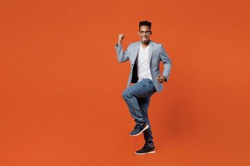 Fototapeta na wymiar Full body young employee business man corporate lawyer in classic formal grey suit shirt glasses work in office doing winner gesture celebrate clenching fists isolated on plain red orange background