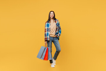 Full body young smiling happy fun cheerful woman wearing casual clothes holding in hand paper package bags after shopping isolated on plain yellow background studio. Black Friday sale buy day concept.